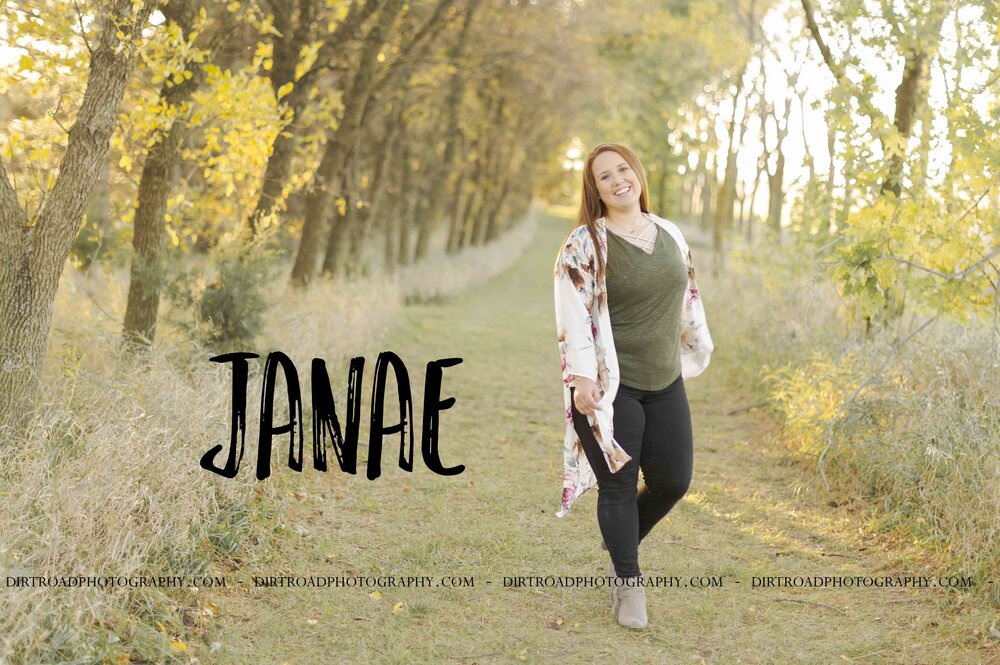 images of high school senior girl named janae of milford, nebraska. she attends milford high school and is part of the class of 2020. photos of teen at softball field, tall green grass path during fall and on brick city streets at sunset in nebraska. girl is dressed in black leggings, green shirt and floral kimono, boutique clothes with brown/tan fringe boots and green striped long sleeved shirt. senior is also wearing purple softball shirt and holding softball bat, softball, baseball glove while standing on a ball field with a water tower in the background. photographer is kelsey homolka nerud of wilber nebraska who specializes in high school senior photography and senior pictures.