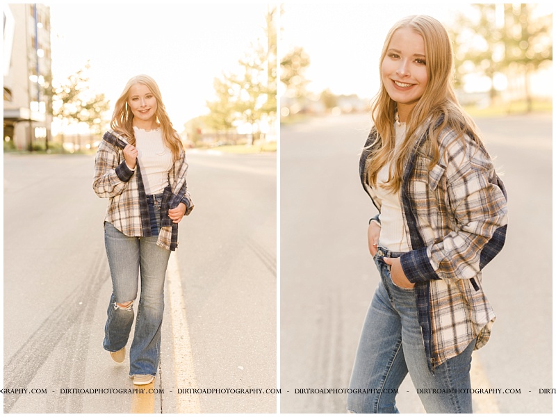 senior picture of girl walking on street with sunset in background. senior picture of girl standing in urban street with buildings on each side wearing flare jeans with white shirt with long blond hair. lincoln southwest high school. nebraska senior photographer located near lincoln, nebraska.