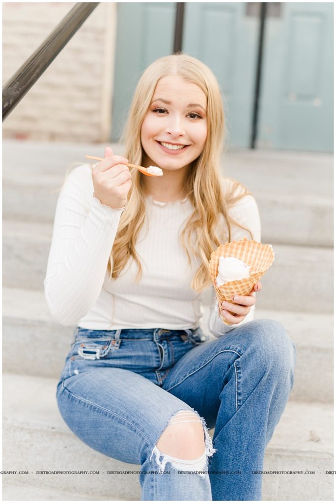 senior picture of girl hold ice cream cone sitting on steps. girl with ice cream for pictures wearing white long sleeve shirt and jeans. long blond hair senior pics. ivonna cone in lincoln nebraska. girl sitting on steps eating ice cream. nebraska senior photographer located near lincoln, nebraska. lincoln southwest high school.