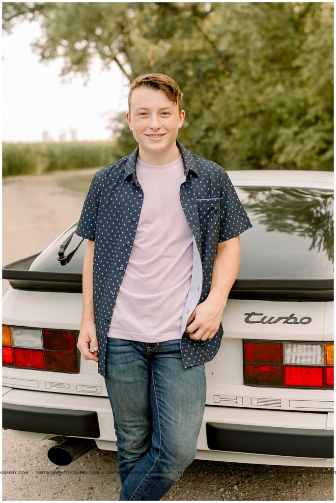crete high school. senior picture of guy with brown hair wearing button up shirt and jeans. photo taken with porsche car and guy leaning on back of car. nebraska senior photographer located near lincoln, nebraska.