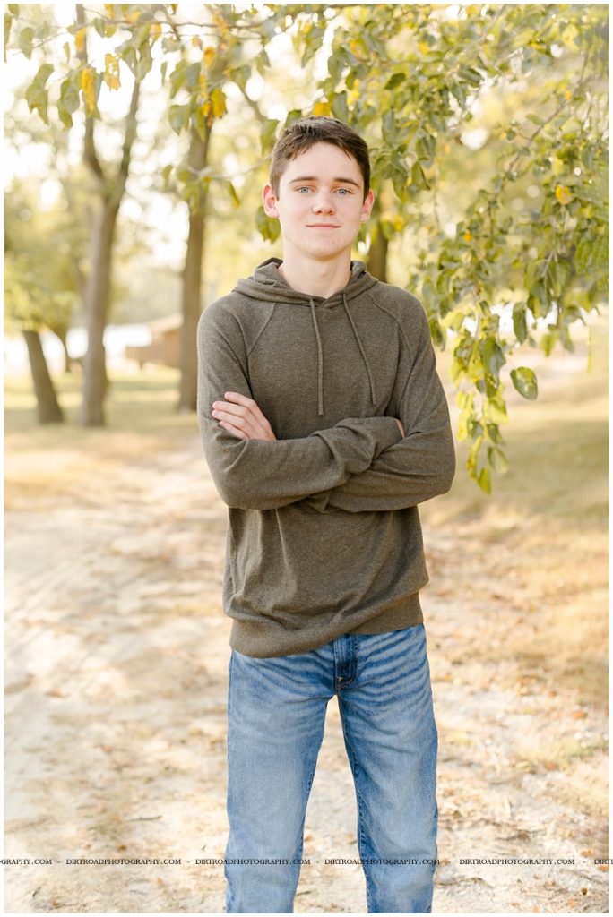senior pictures of boy sitting standing by tree with sun shining on him. senior boy wearing a green long sleeve shirt and jeans. senior pictures of ashland-greenwood high school senior. pictures taken by dirt road photography, lincoln nebraska best senior photographer.