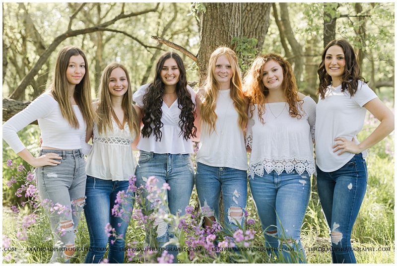 picture of group senior girls taken standing in tall purple flowers with trees near wilber, nebraska. senior picture of girls wearing white tank tops with blue jeans standing in purple wildflowers. senior picture taken at sunset during the spring in nebraska. pictures taken by dirt road photography, lincoln nebraska best senior photographer.
