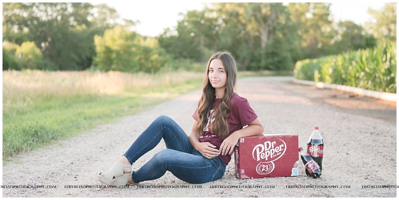 senior pictures of a girl from hebron, nebraska taken on a gravel road with dr. pepper. girl wearing dr. pepper tshirt.