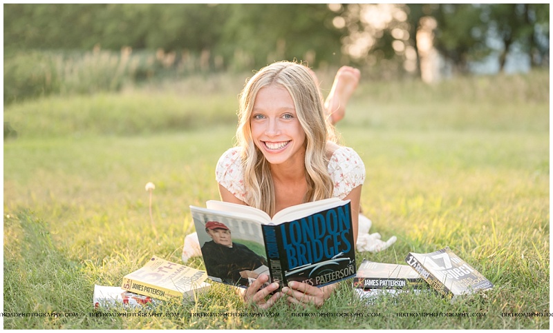 Senior laying in grass with James Patterson books at sunset