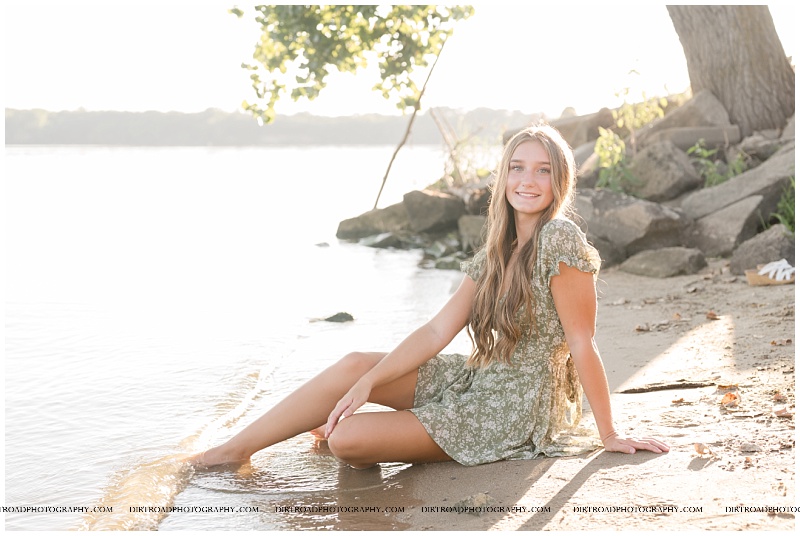 Senior girl lying along the shoreline at Branched Oak Lake during golden hour in Nebraska